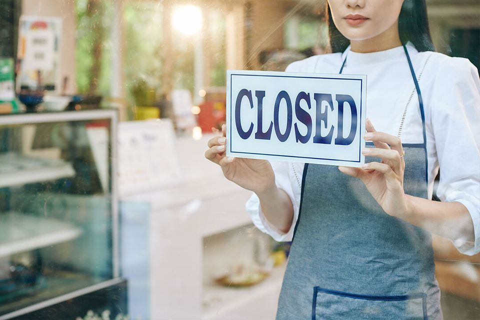 Woman in a retail store frowning as she hangs a closed sign.